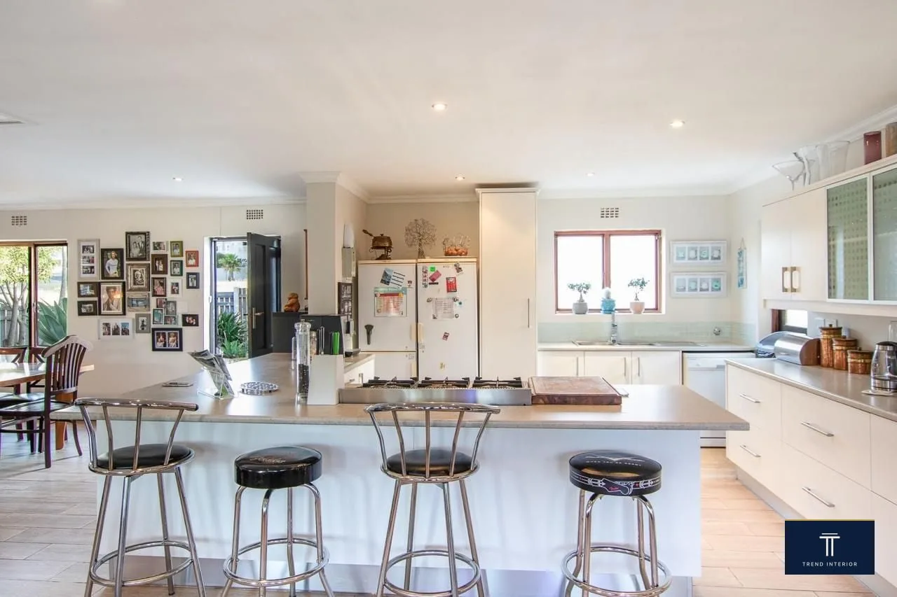Custom kitchen with central island, cream cabinetry, integrated gas hob, bar seating, and dining nook visible beyond.