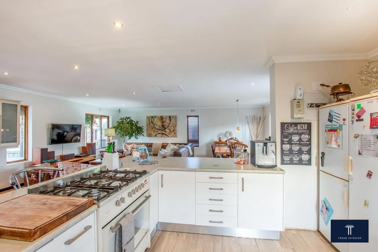 Open-plan kitchen and living area with custom cabinetry, gas range, frosted glass uppers, granite-look counters and a coffee station.