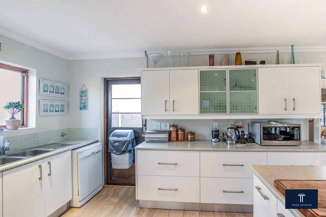 Scullery off the main kitchen with custom cabinetry, integrated dishwasher, double sink, frosted glass uppers and tile splashback.